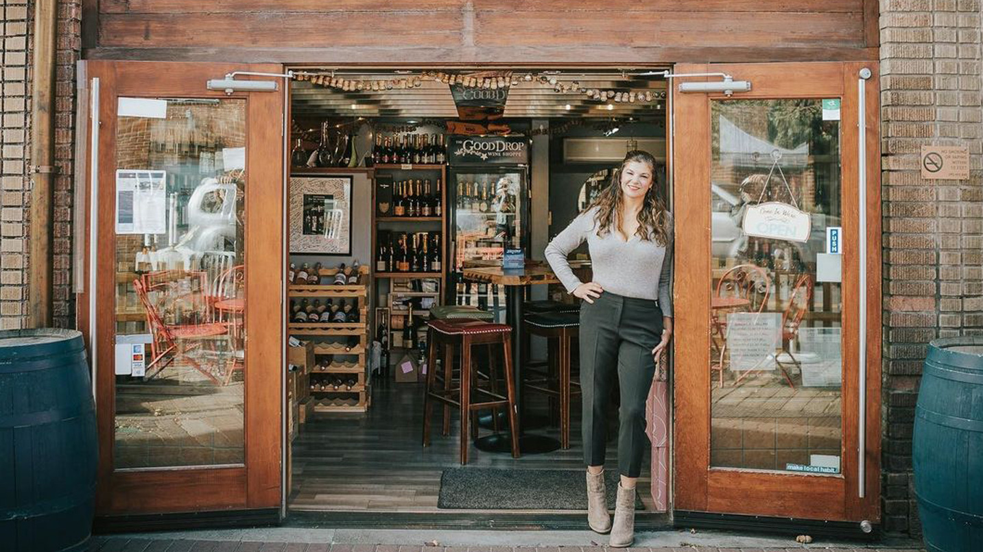 A woman stands in the doorway of a wine shop.