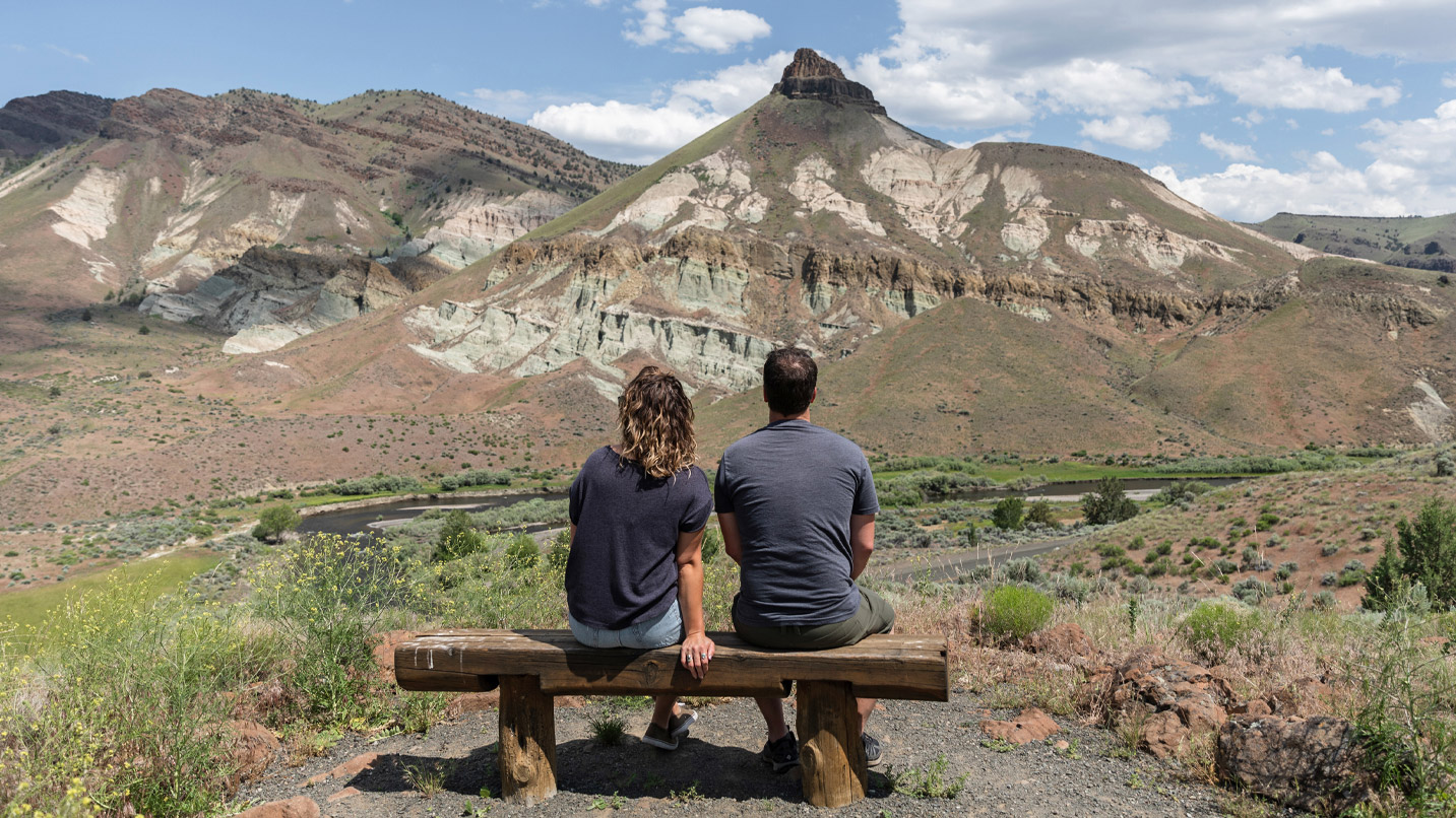Two people sit on a log bench overlooking a view of SheepRock.