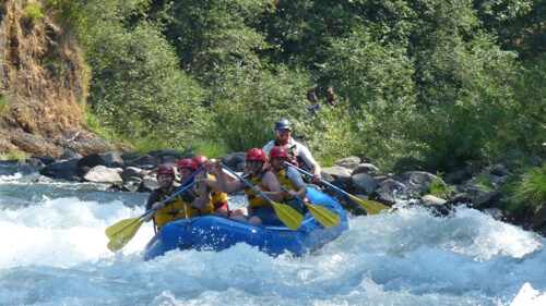 A group of people in safety gear rafting a rushing river.