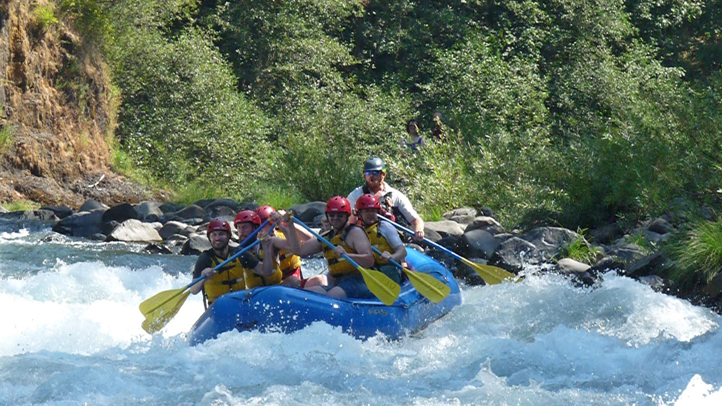 A group of people in safety gear rafting a rushing river.
