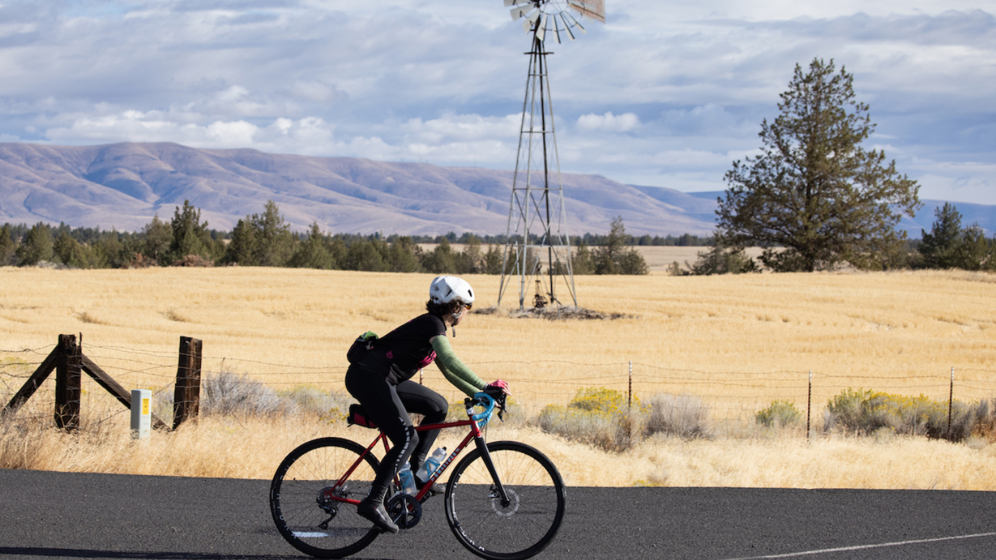 Cyclist on road with rolling fields and windmill in background