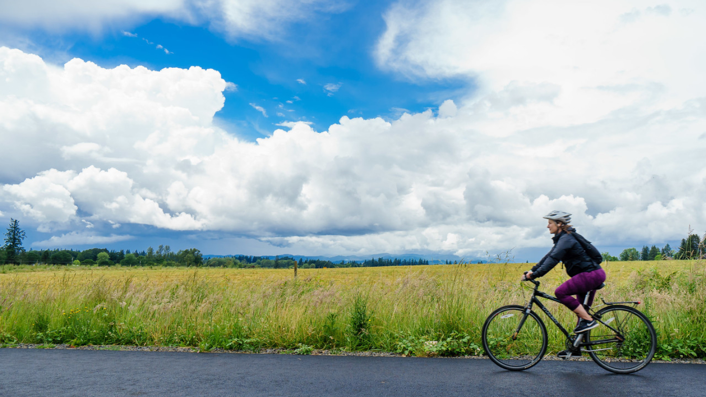 Woman rides bike with grass, blue sky and clouds