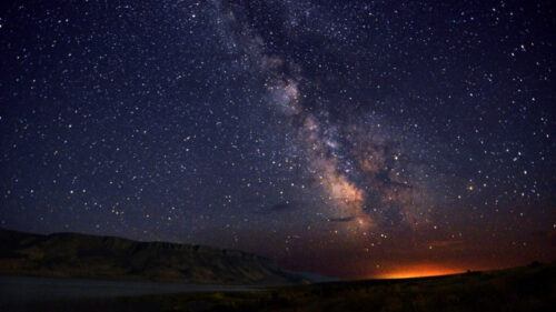 dark sky with stars over an orange glow on the landscape