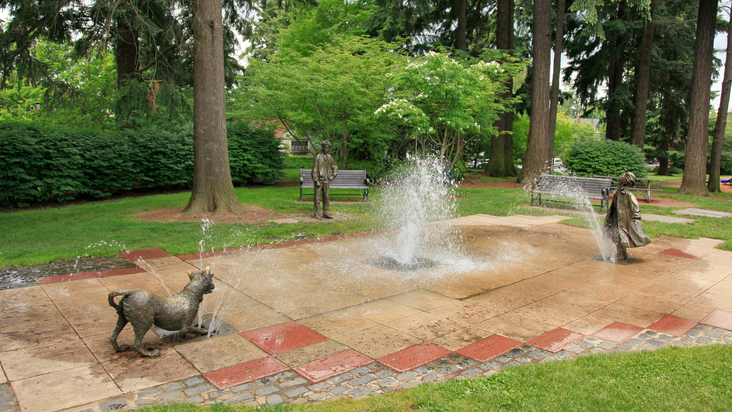 A water fountain at a park with small bronze statues of a dog, and a small girl and boy.