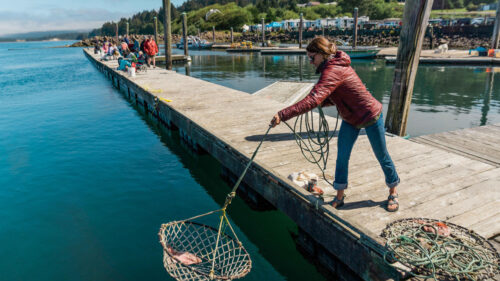 A woman casts a crab net into the water off a dock.