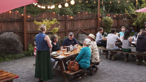 Outside dining area with picnic tables, shading umbrellas and string lights.