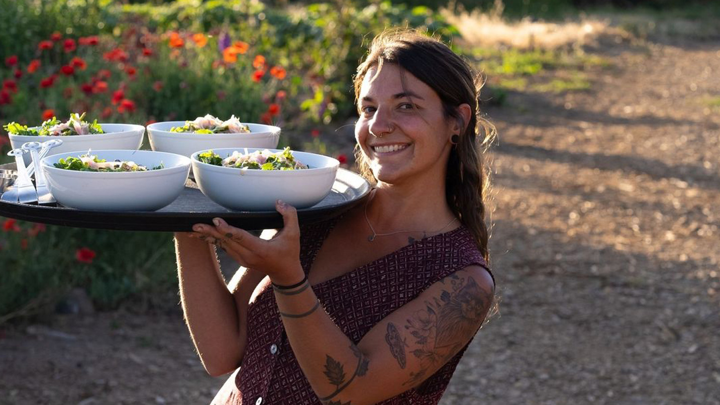 A woman smiling holding up a tray of salads on a farm restaurant.