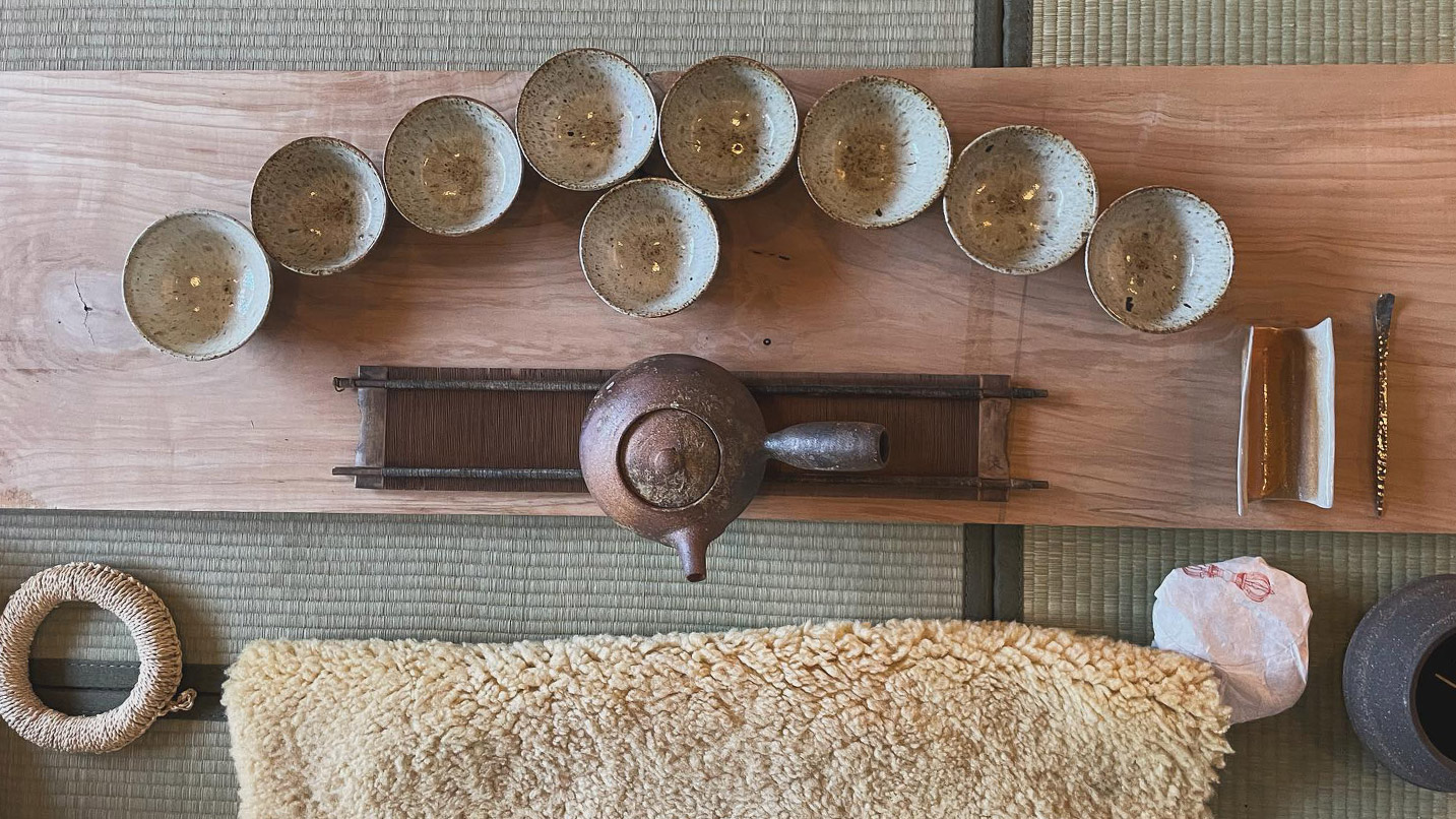Rustic tea kettle and tea cups lined up in a traditional Buddhist style.
