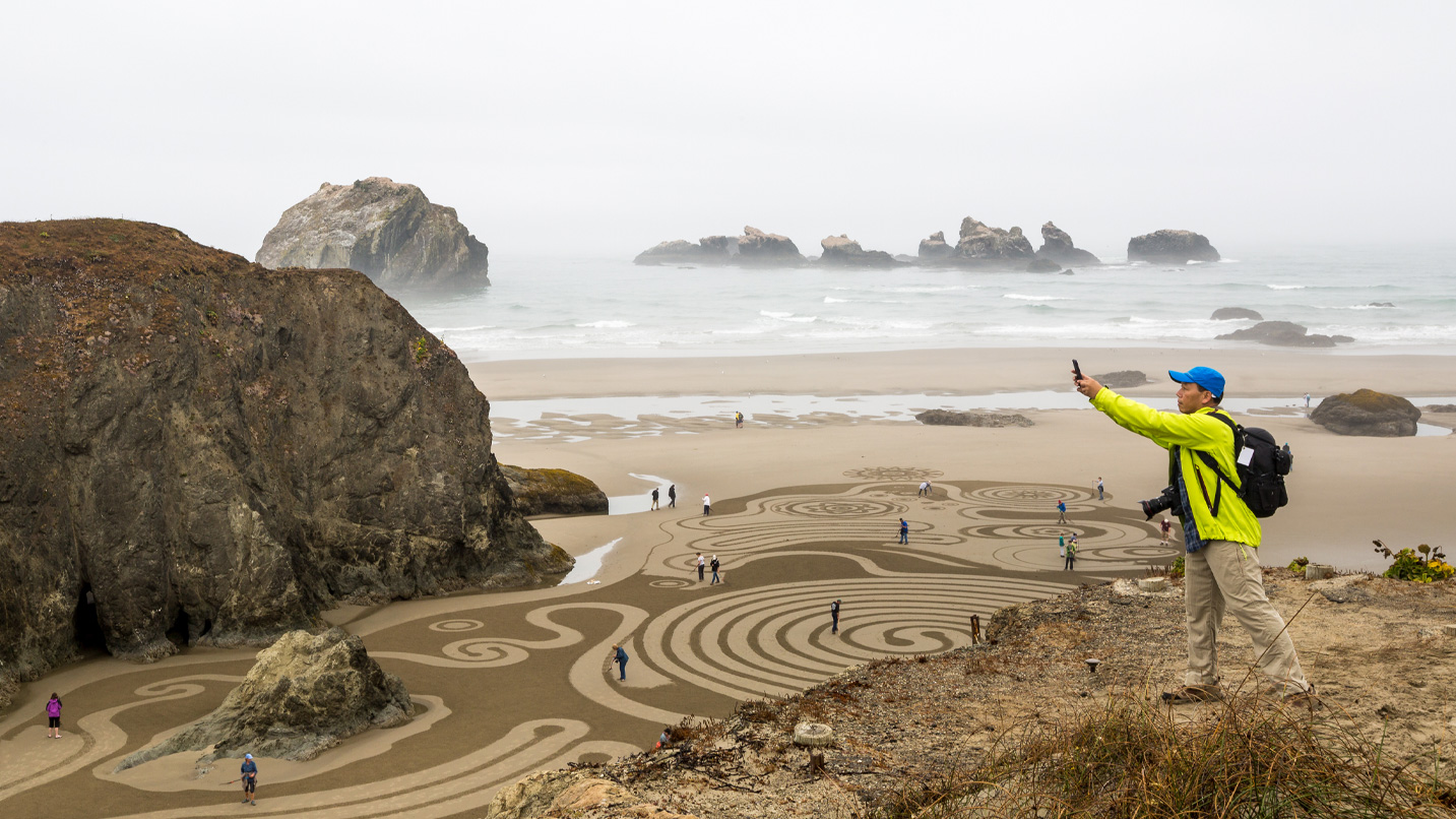 A person taking a photo of the elaborate sand art on the beach in Bandon.