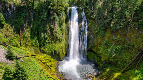 A tall waterfall pours down to a small body of water surrounded by cliffsides full of green vegetation.