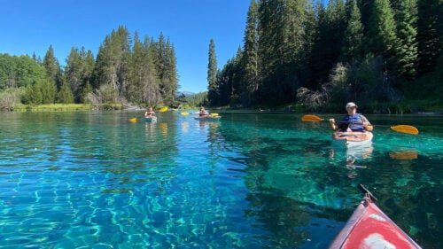 People kayaking on a calm body of teal blue water.