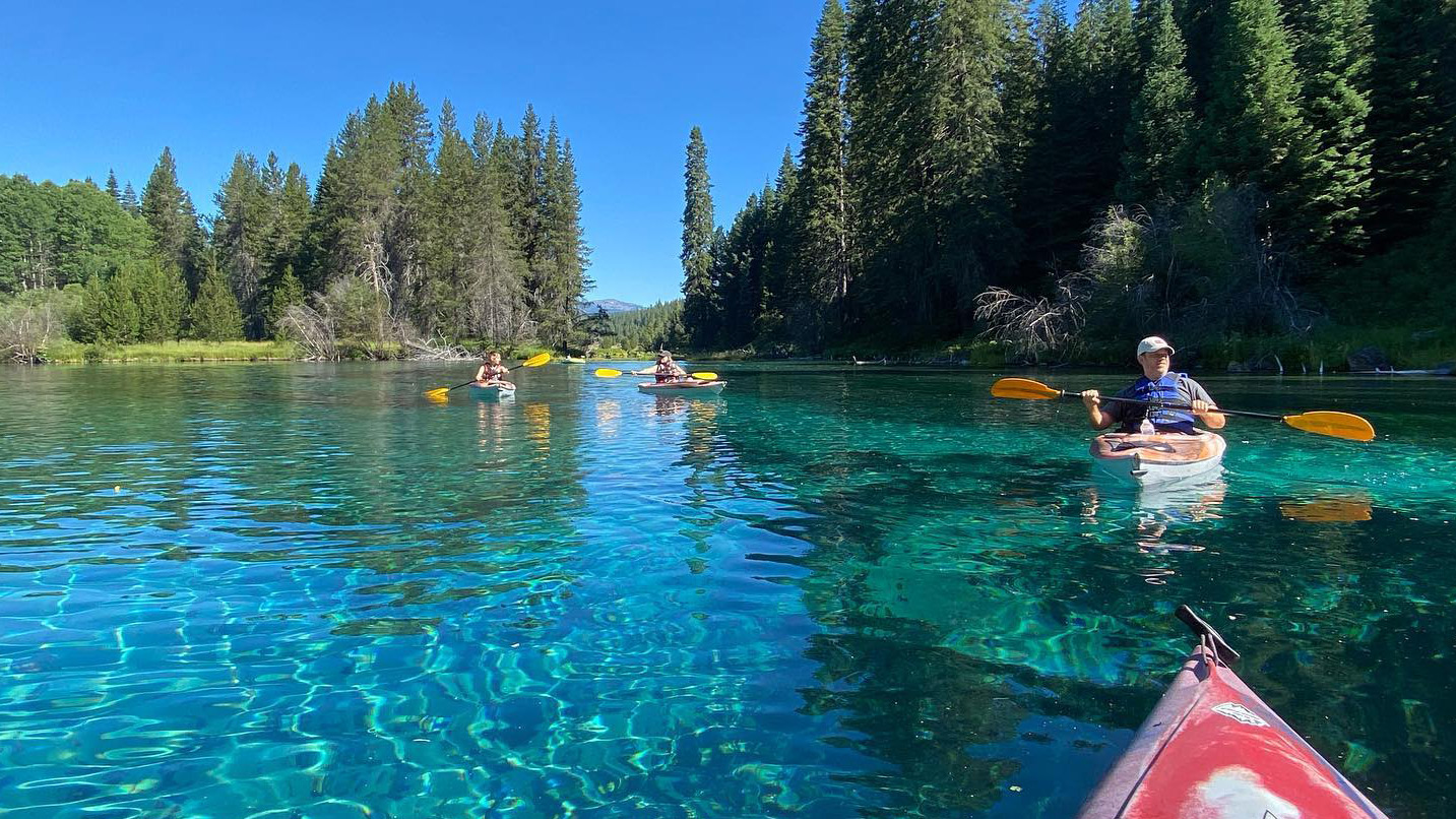 People kayaking on a calm body of teal blue water.