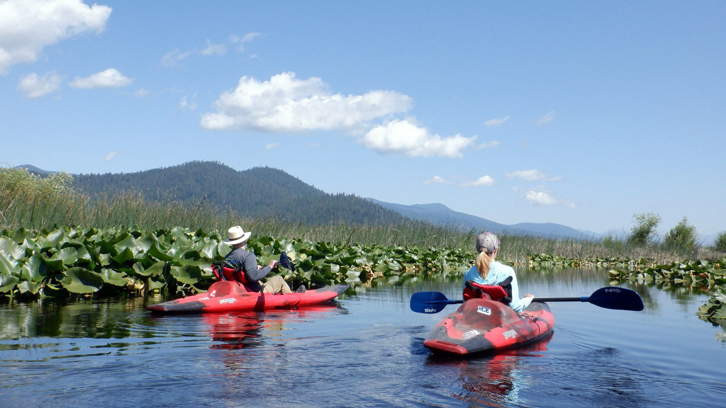 2 people in kayaks rest their paddles on their boats while looking at hills off into the distance.
