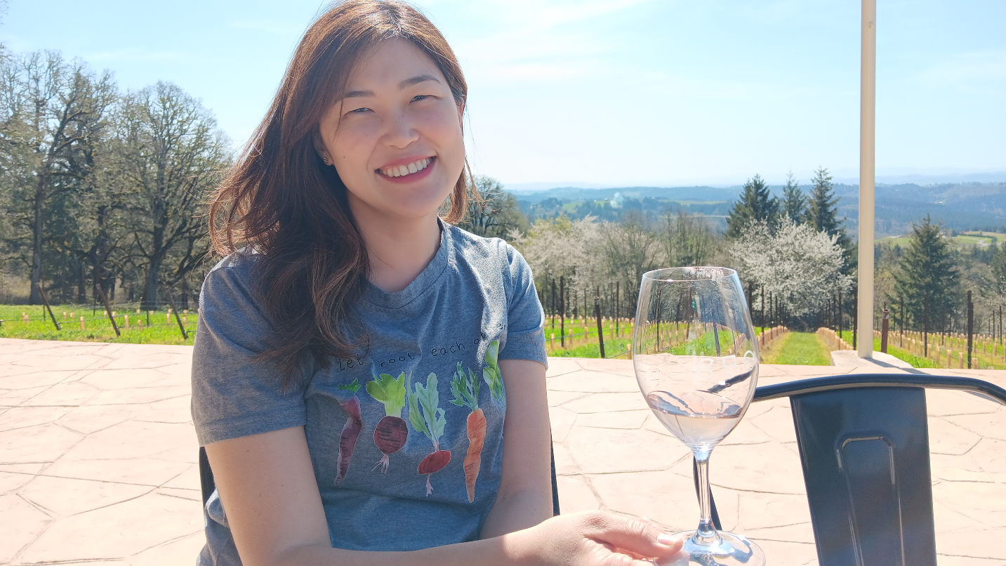 Woman smiles holding wine glass with vineyard in background