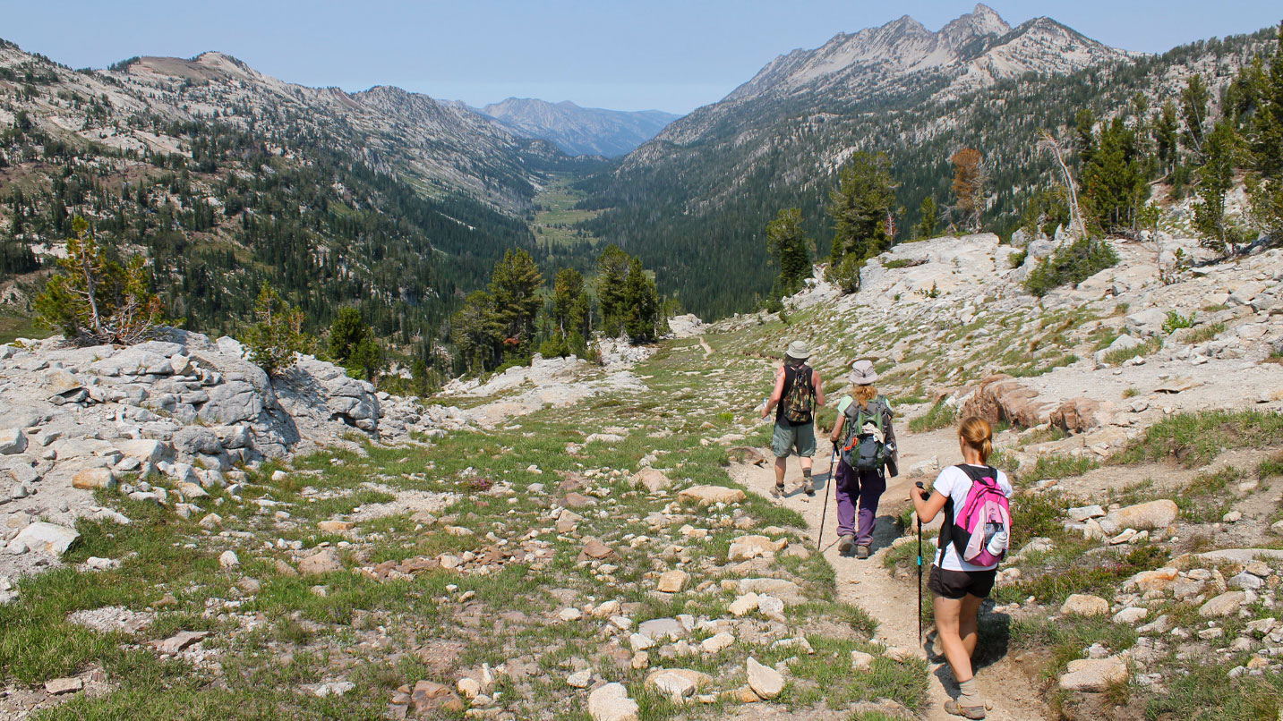 Three people on a trail with views of a forested canyon.