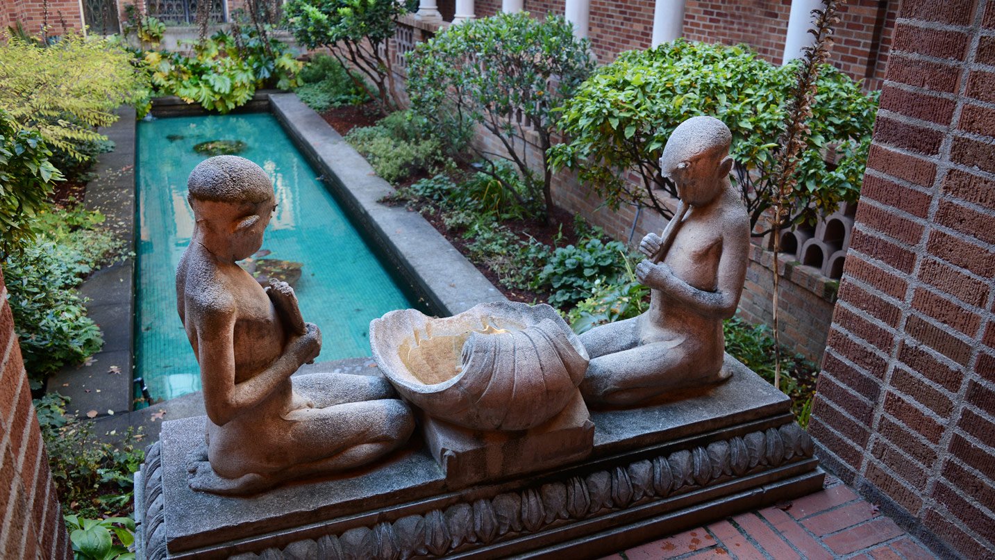 Two kneeling sculptures next to a fountain in an outdoor courtyard.
