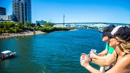 People with drinks in hand look over a boat's railing at the city in the distance.