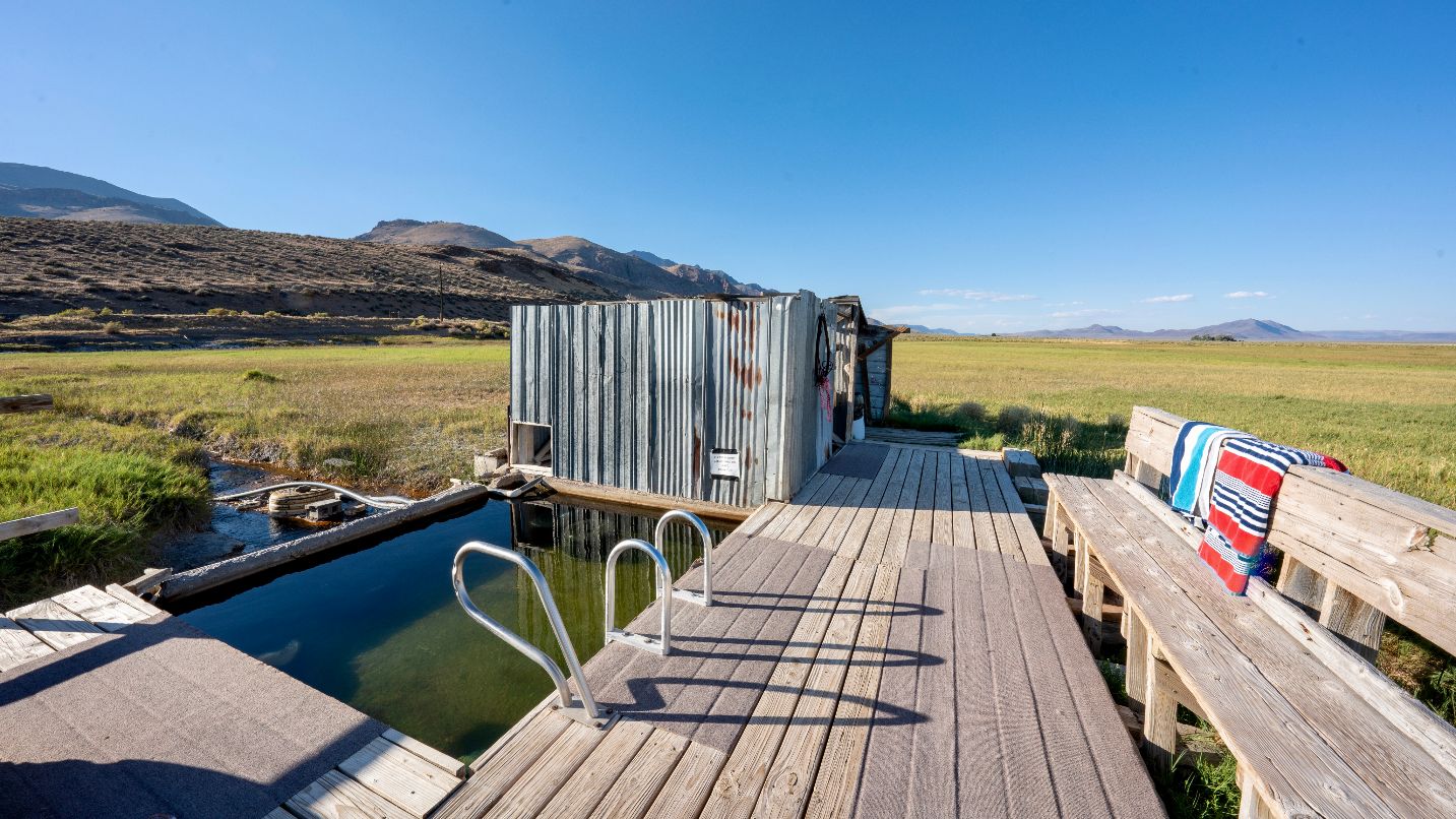Wooden deck, tin shed and hot spring with grass and mountain vistas in background