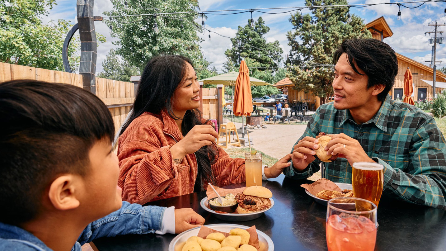 A family sits outside with food and drinks on a table.