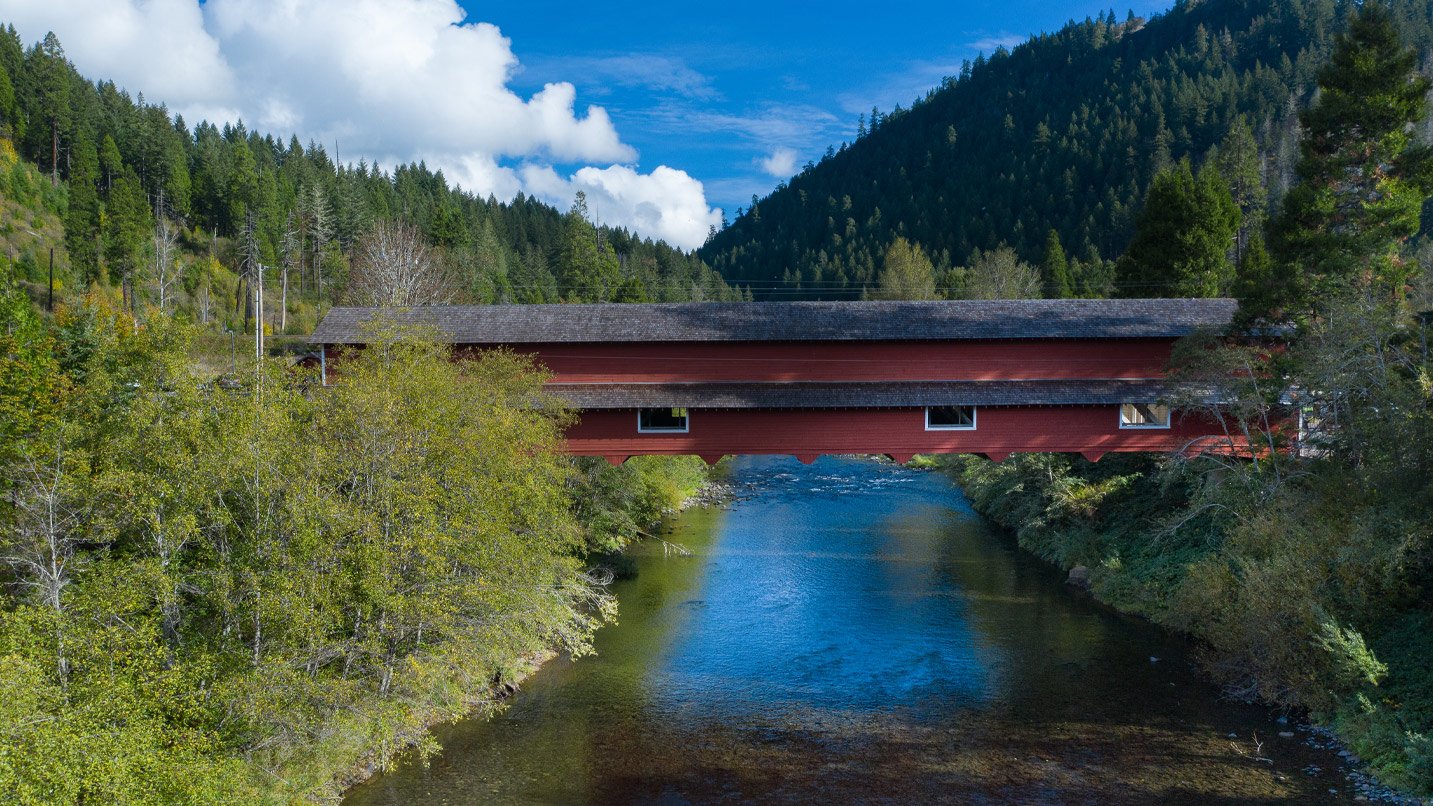 A long, bright red roofed structured bridge spanning over a river.