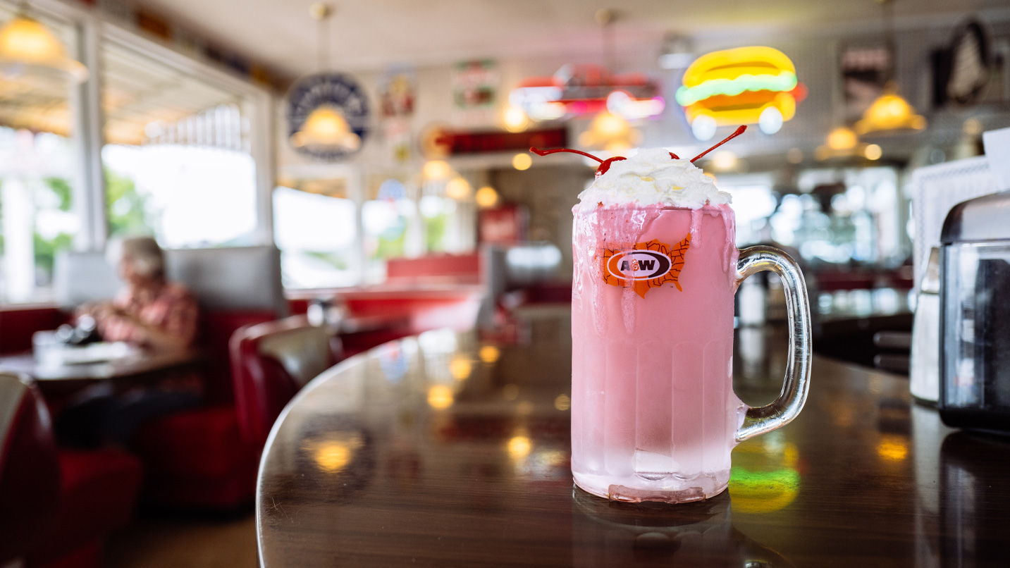 A tall glass of a frosty pink drink topped with whipped cream on a diner counter.