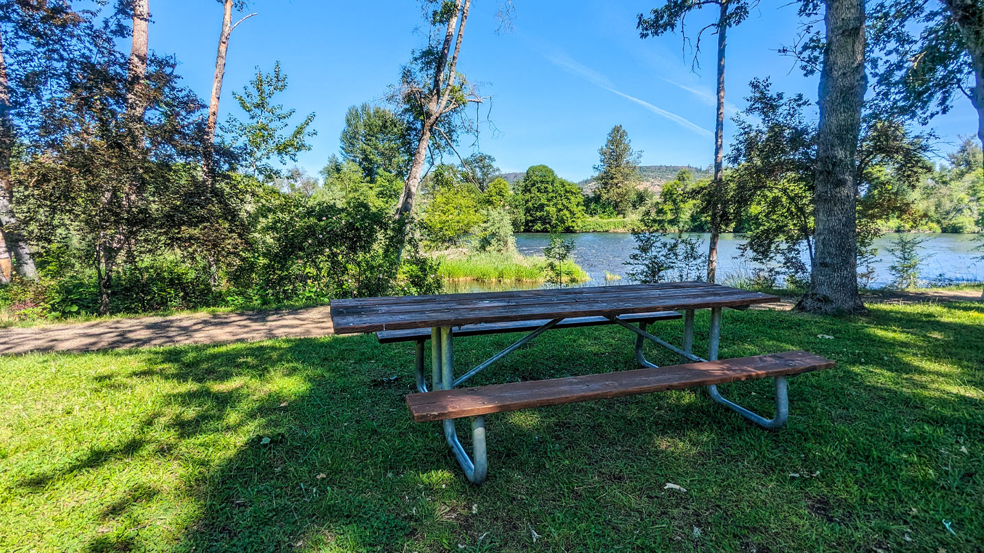 A picnic bench on a grassy area with views of a river.