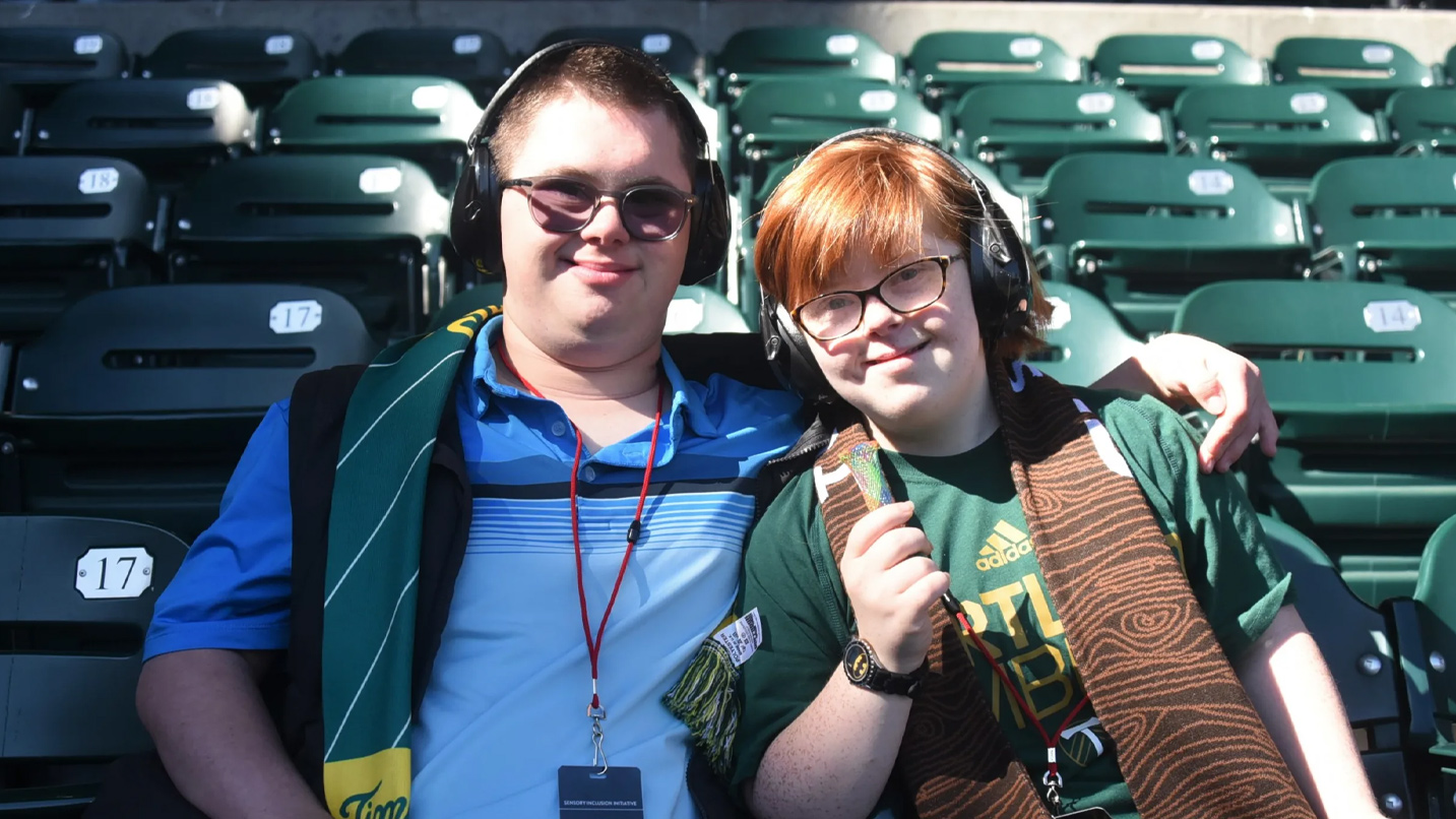 A couple with Downs Syndrome smiling at stadium seating at Providence Park.