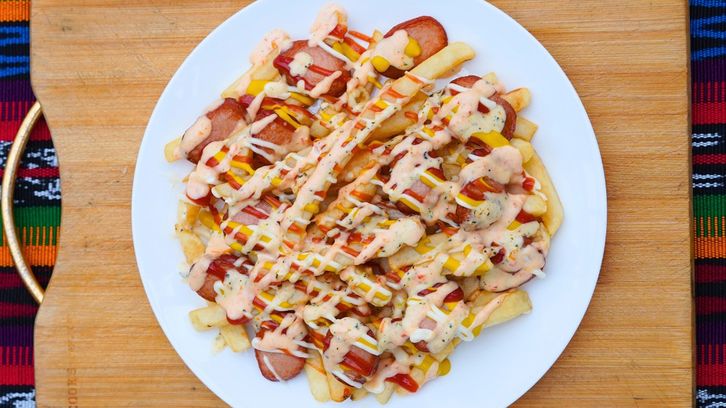 A plate of french fries and sliced sausage covered with various sauces.