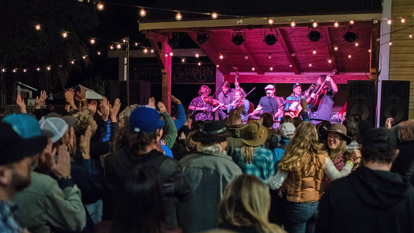 A small outdoor stage at night with lights strung above a crowd of people.