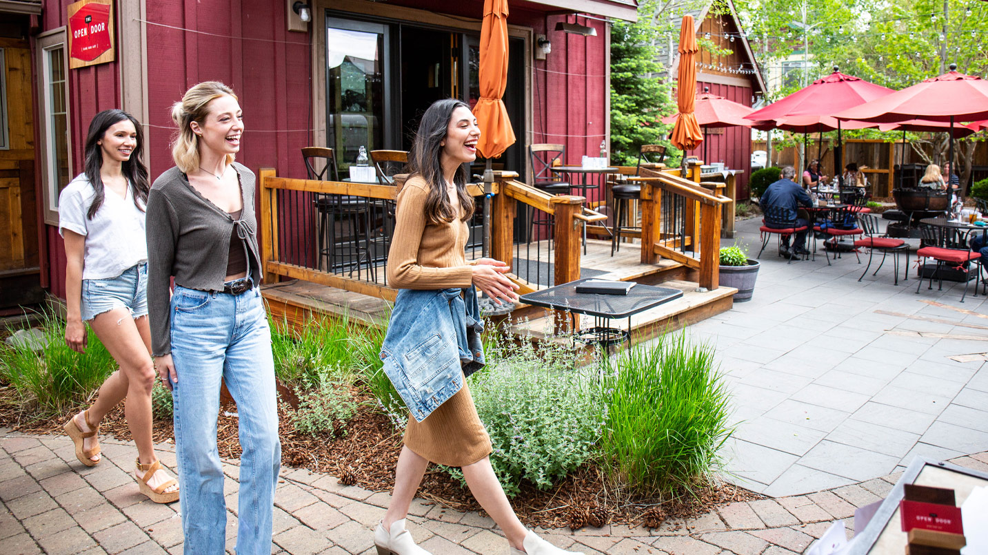 Two people walk into a large open patio with umbrella-covered tables.