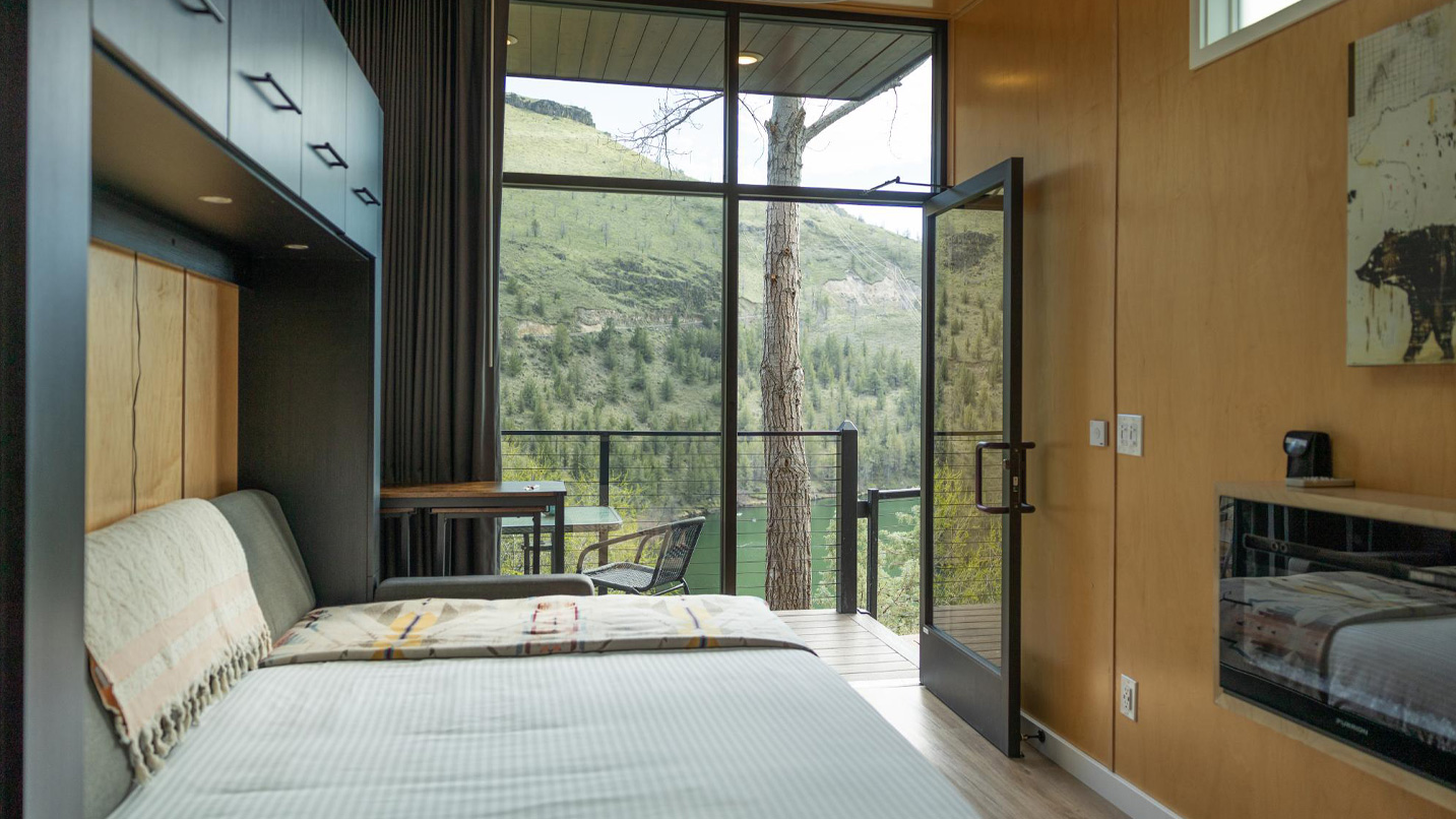 Interior of a tiny home, fitted with a full-sized murphy bed with views of Lake Simtutus through its floor-length windows.