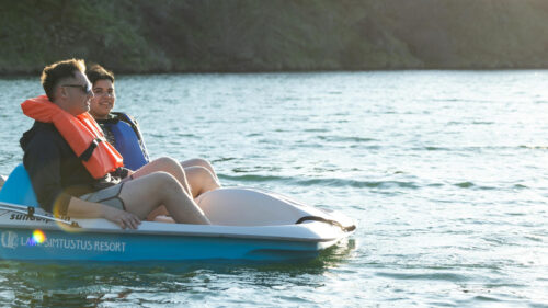 Two people on a pedal boat wearing life jackets on a lake.