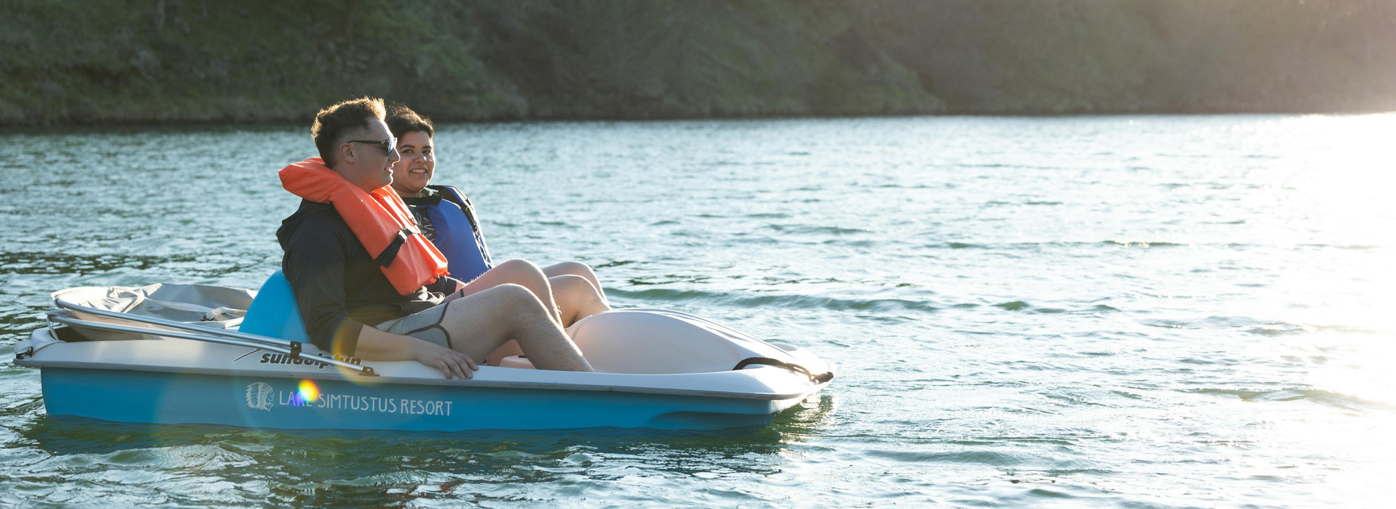 Two people on a pedal boat wearing life jackets on a lake.