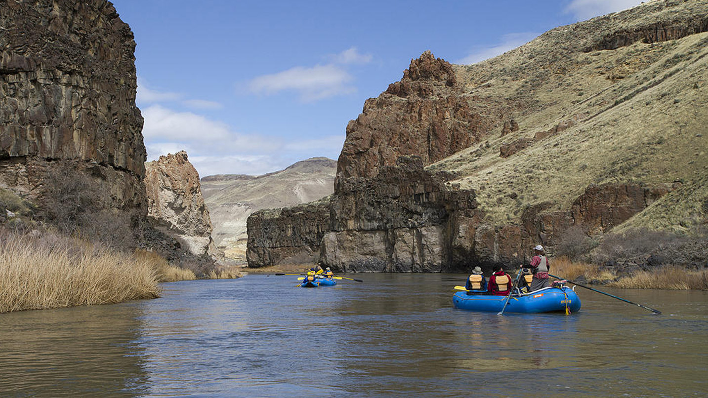 People rafting down a calm portion of the Owyhee River through canyons.