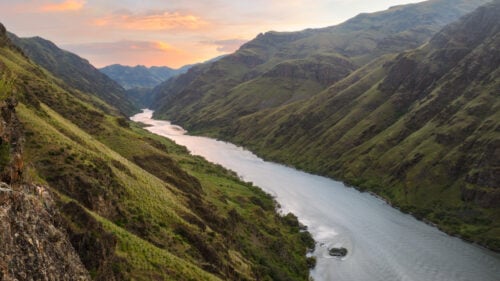 A river coursing through a green-filled canyon during sunset.