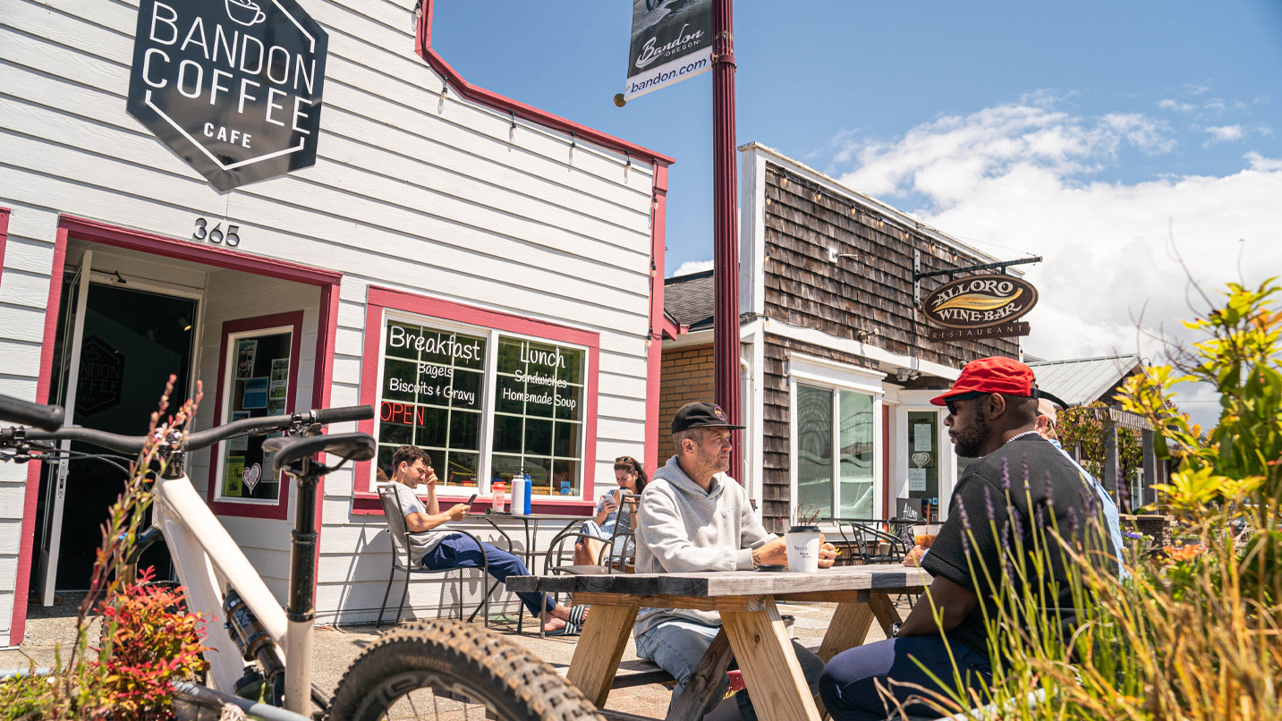 People sit at an outdoor picnic table in front of a coffee shop.