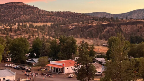 A small building sits in a valley surrounded by hills at sunset.