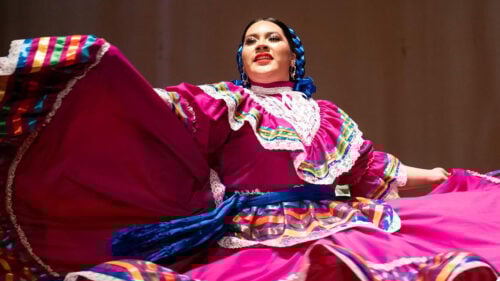 A girl in traditional Mexican dress and hair ribbons flaring her skirt in a dance.