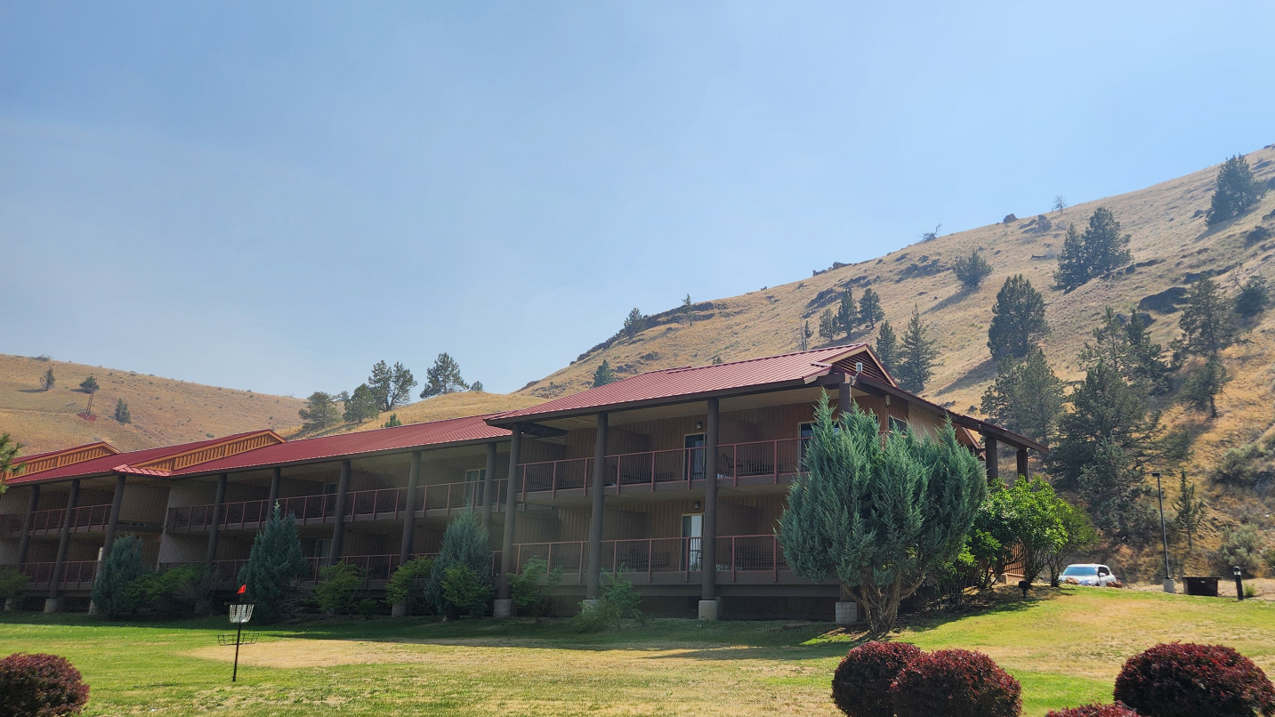 Exterior of a two-story hotel with green hills in background and grass in foreground