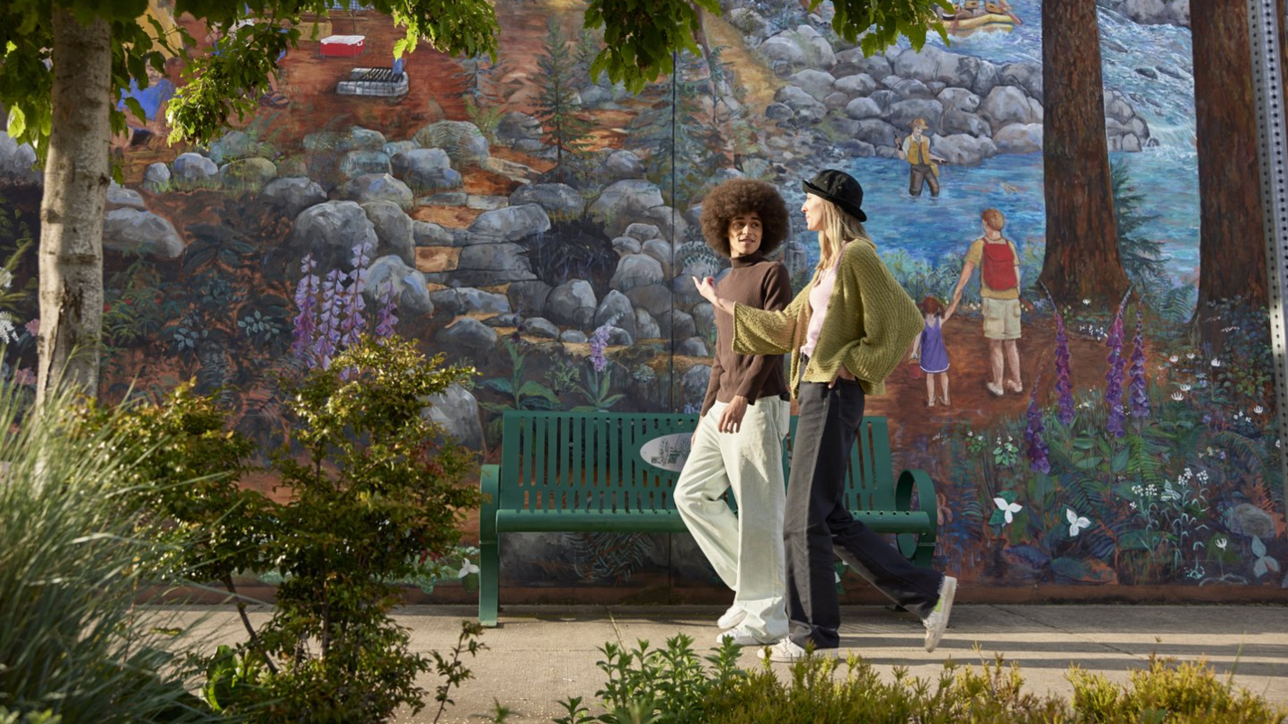 Man and woman walk next to a colorful mural with greenery.