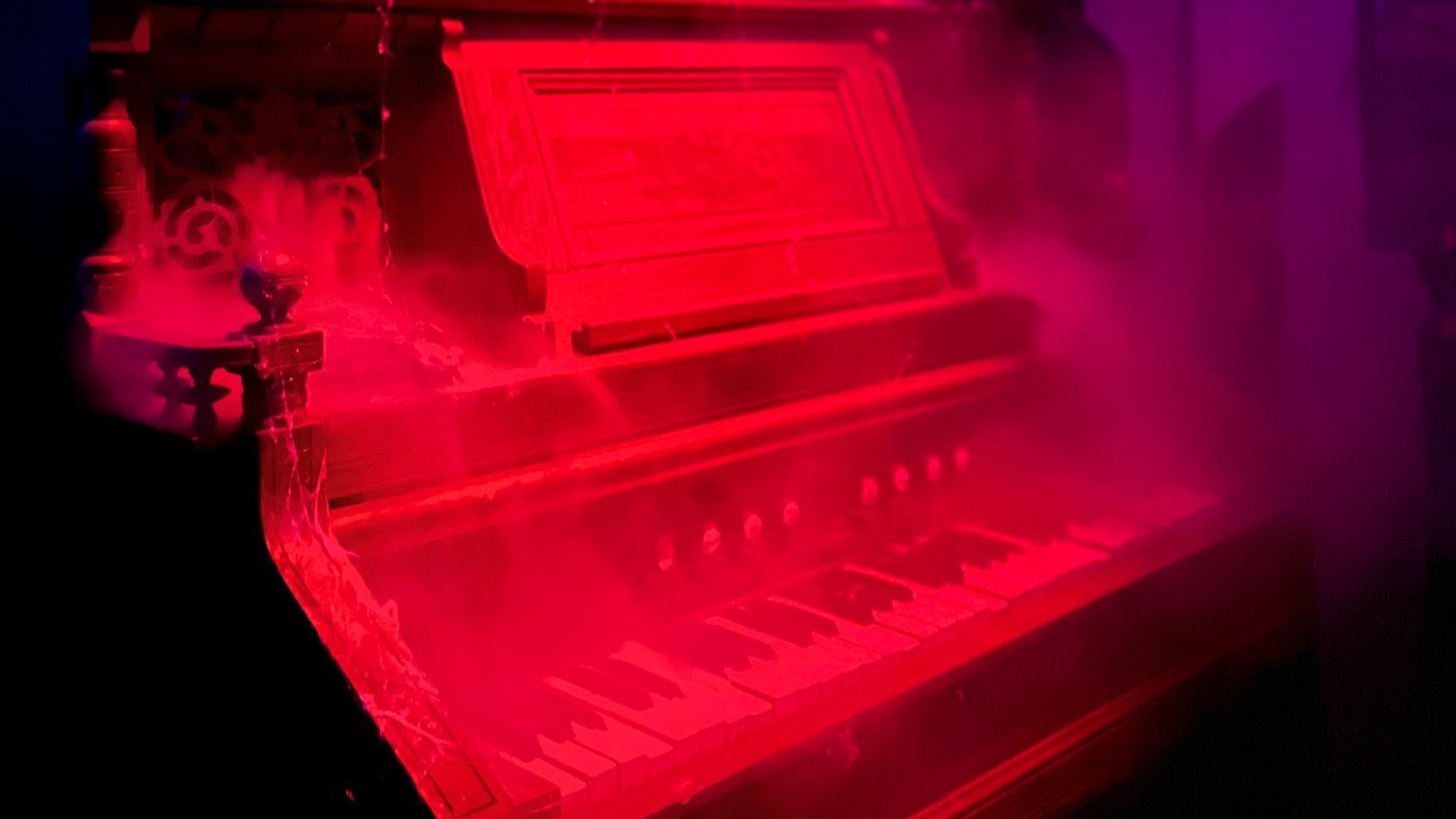 A piano shrouded in smoke lit under red light.