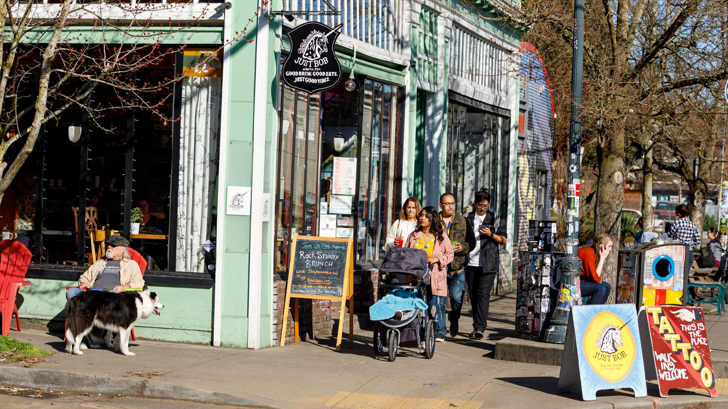 People walk with a stroller and drinks in hand along busy sidewalk