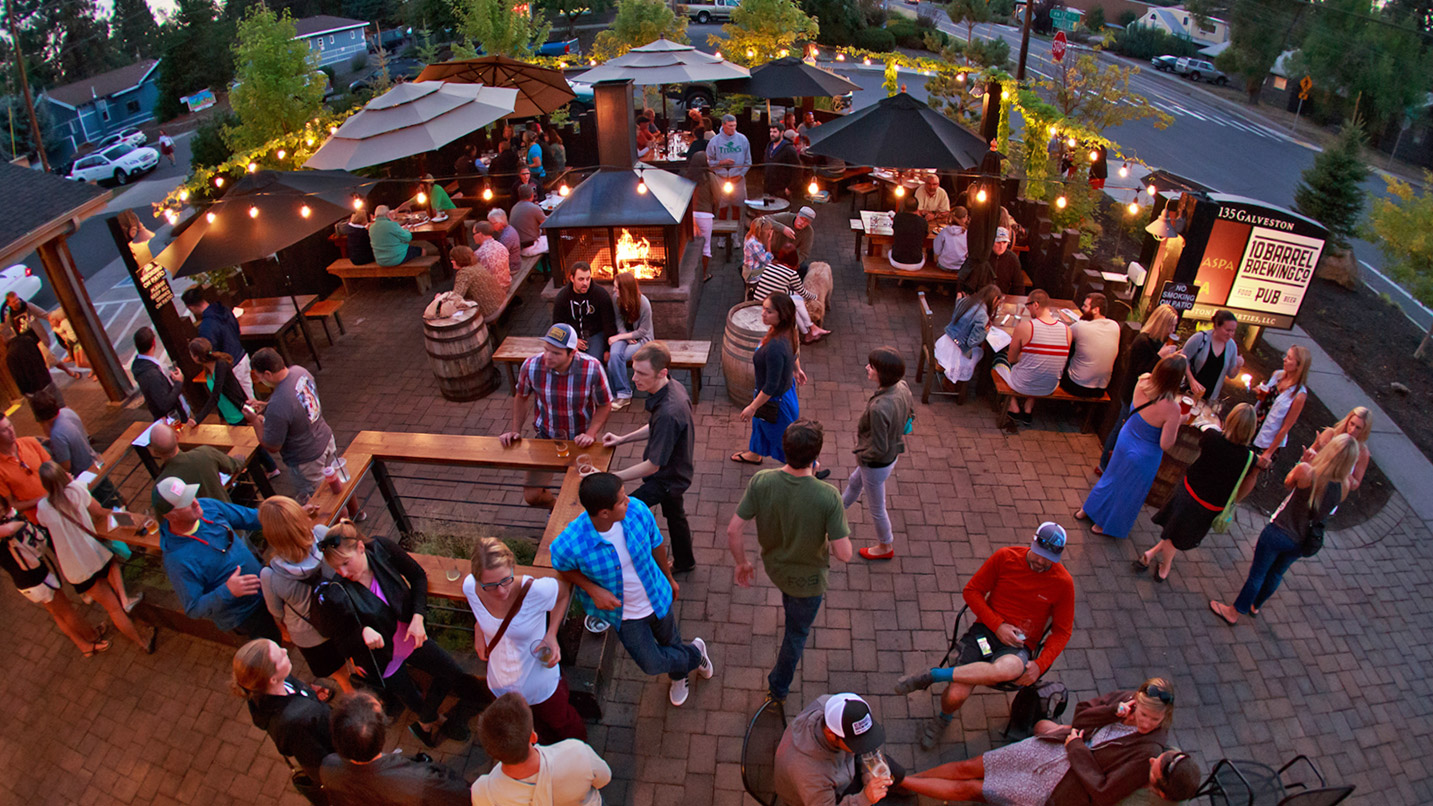 A brewery's outdoor seating area filled with people sitting and milling around.