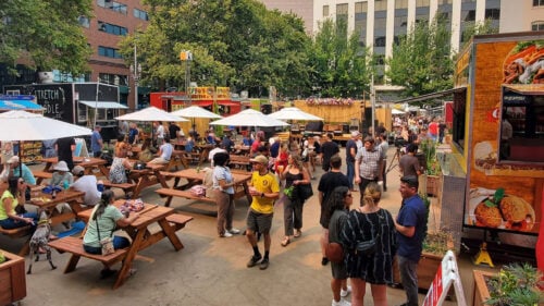 A large and busy food cart pod with picnic tables for outdoor seating.