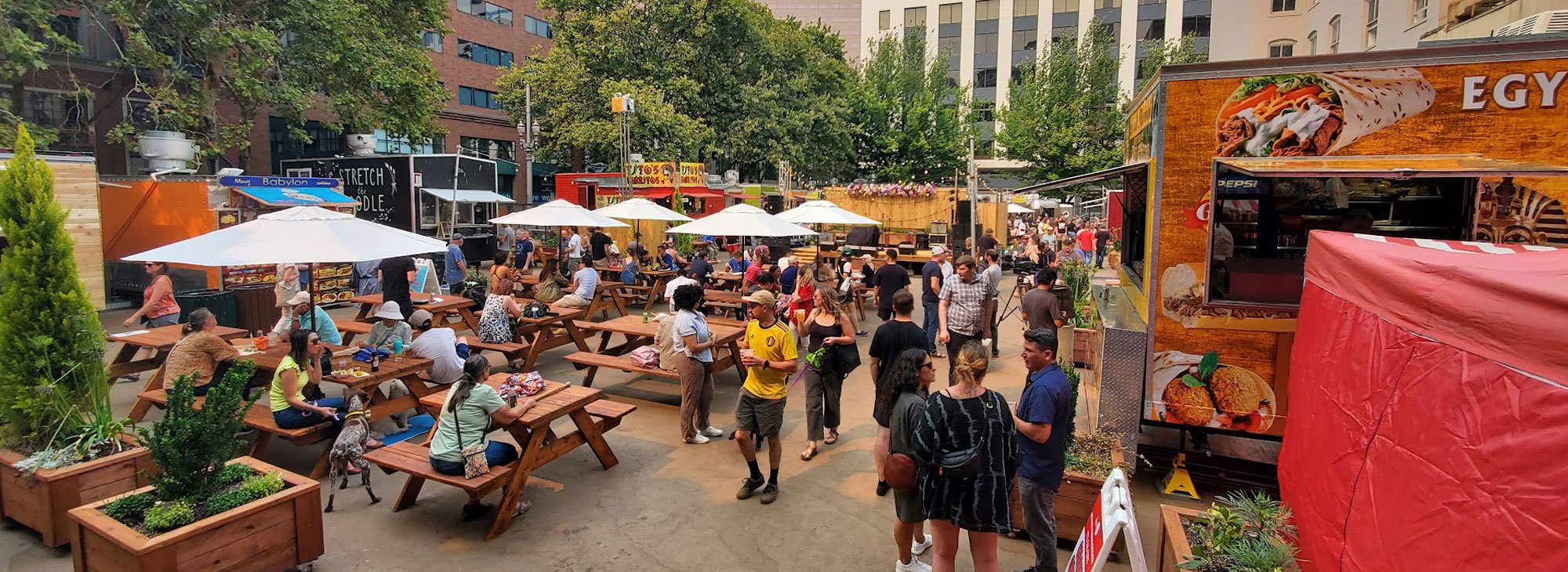 A large and busy food cart pod with picnic tables for outdoor seating.