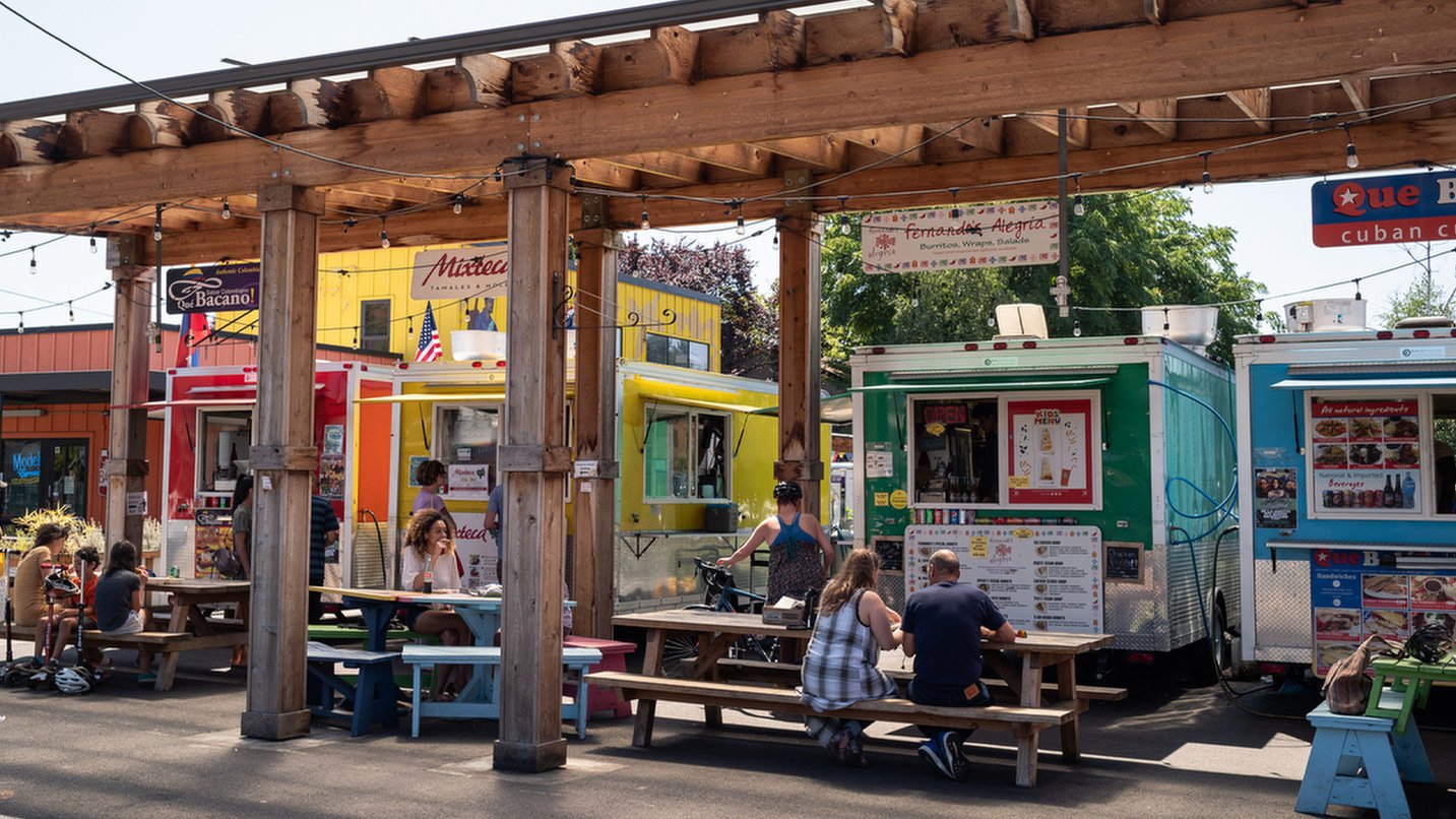 A strip of colorful food carts, with picnic tables nearby for seating.