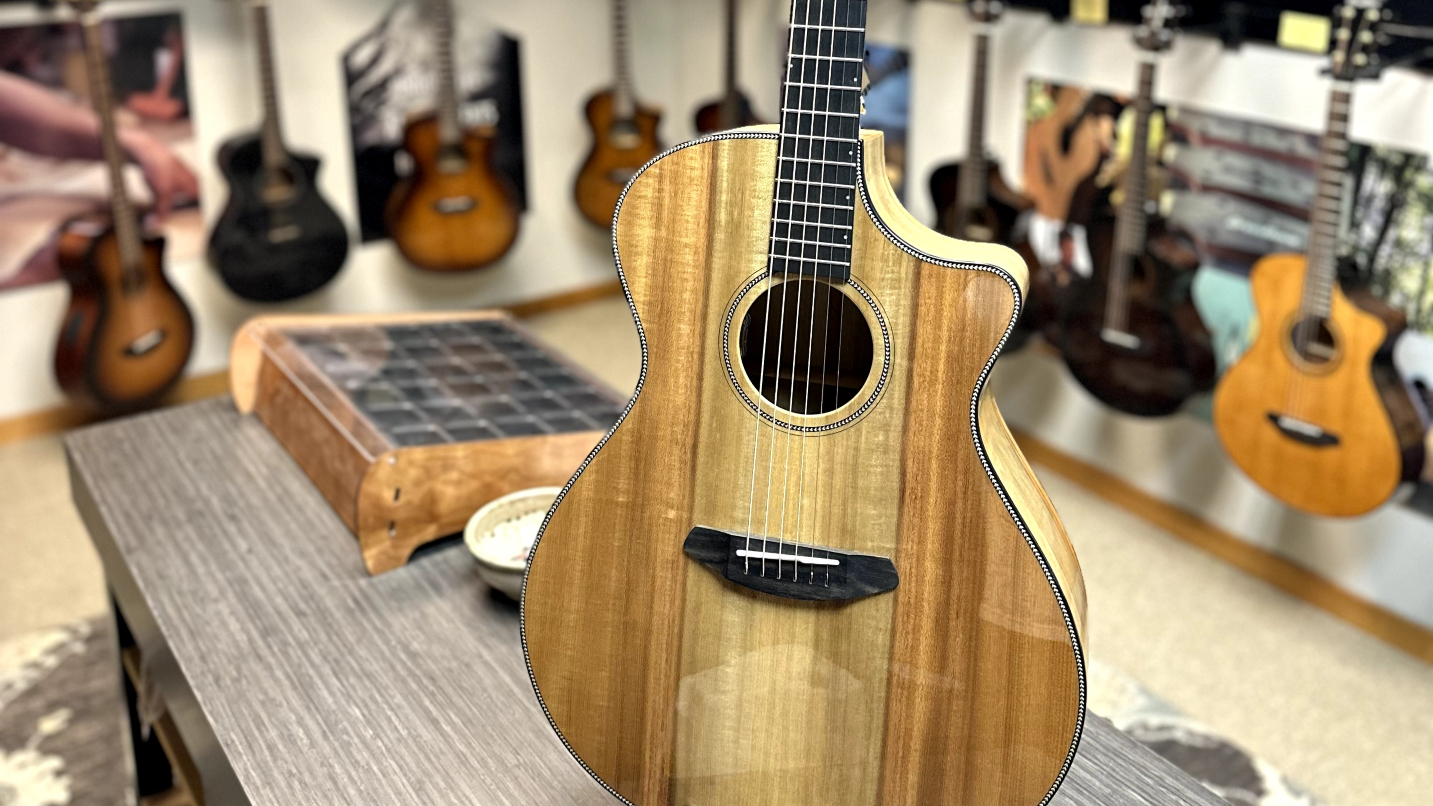 Close-up of light wood guitar with other guitars on wall in background
