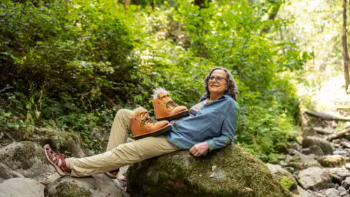 Woman lounges on rock with trees in background and puppet boots on her stomach