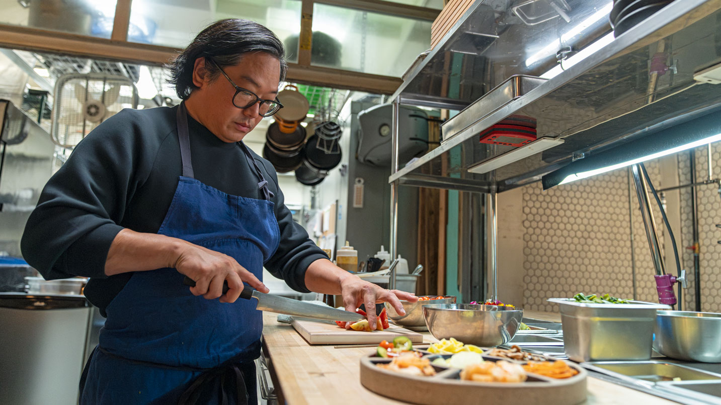 Man in blue apron cuts food on cutting board