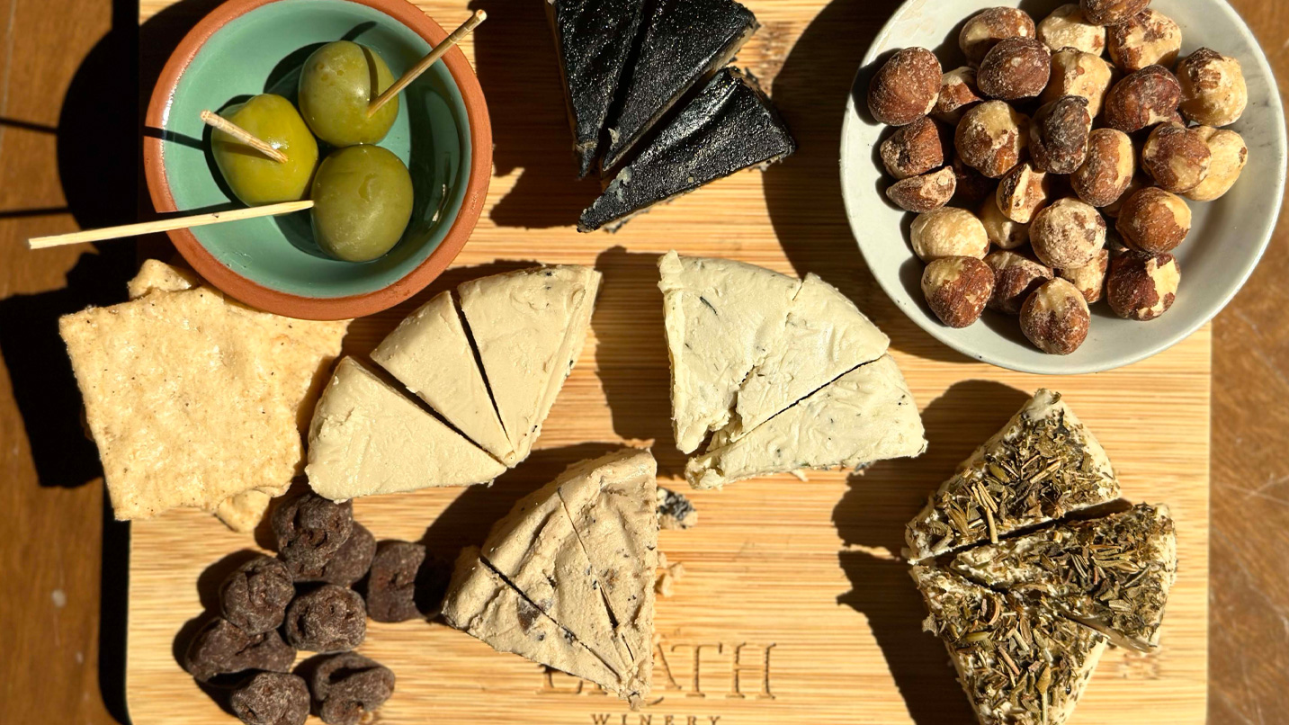 Wedges of cheese, nuts and olives on a wooden cutting board.